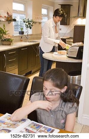 Girl reading a comic book with her mother preparing food in the background View Large Photo Image Stock Image - Girl reading a comic book with her mother preparing food in the background. Fotosearch