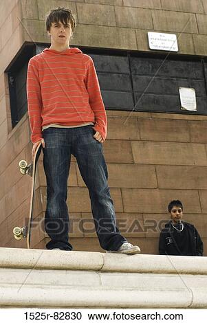 Stock Image - Low angle view of a teenage boy holding a skateboard. Fotosearch