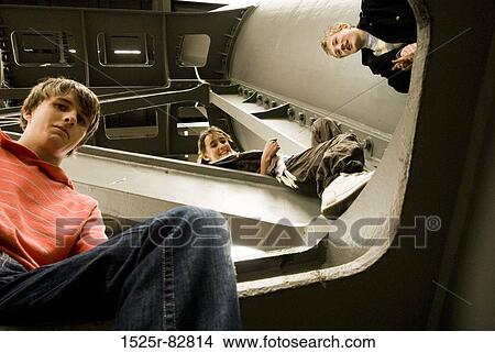 Picture - Low angle view of two teenage boys and a teenage girl sitting on a bridge. Fotosearch