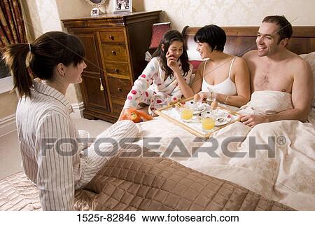 Mid adult couple with their daughter sitting on the bed with a young woman sitting in front of them View Large Photo Image Stock Photograph - Mid adult couple with their daughter sitting on the bed with a young woman sitting in front of them. Fotosearch