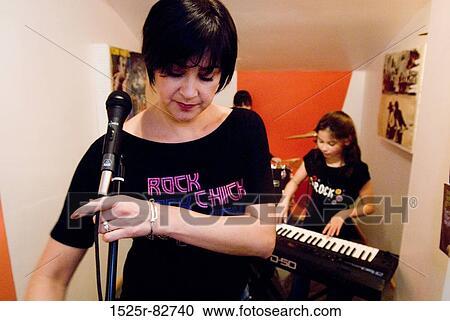 Mid adult woman adjusting a microphone with her daughter playing a synthesizer behind her View Large Photo Image Stock Image - Mid adult woman adjusting a microphone with her daughter playing a synthesizer behind her. Fotosearch
