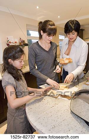 Stock Photo - Mid adult woman with her two daughters preparing sandwiches. Fotosearch