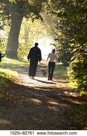 Stock Image - Rear view of a man and a woman walking on a dirt road in a park. Fotosearch