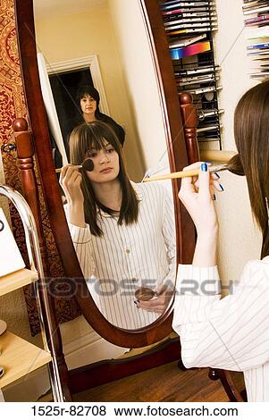 Stock Photo - Reflection of a teenage girl applying make-up to her face with her mother standing behind her. Fotosearch