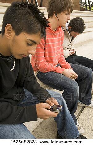 Teenage boy using a mobile phone with two other teenage boys sitting beside him View Large Photo Image Stock Photo - Teenage boy using a mobile phone with two other teenage boys sitting beside him. Fotosearch