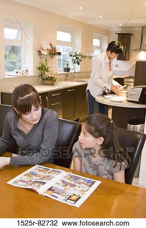Teenage girl and a girl sitting at a table with a mid adult woman preparing food in the background View Large Photo Image Stock Image - Teenage girl and a girl sitting at a table with a mid adult woman preparing food in the background. Fotosearch