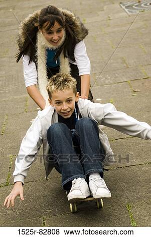 Teenage girl pushing a boy sitting on a skateboard View Large Photo Image Stock Photo - Teenage girl pushing a boy sitting on a skateboard. Fotosearch