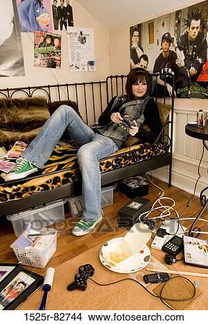 Picture - Teenage girl reclining on a bed and playing a video game. Fotosearch