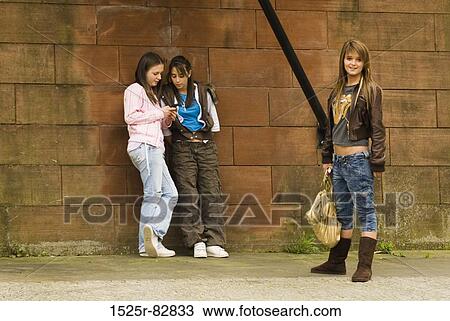Stock Image - Three teenage girls standing in front of a stone wall. Fotosearch