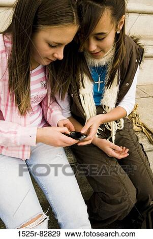 Two teenage girls holding a mobile phone View Large Photo Image Stock Photo - Two teenage girls holding a mobile phone. Fotosearch