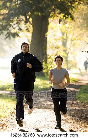 Stock Image - Young couple jogging on a dirt road in a park. Fotosearch