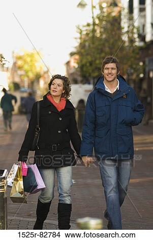 Young man holding the hand of a young woman carrying shopping bags View Large Photo Image Picture - Young man holding the hand of a young woman carrying shopping bags. Fotosearch