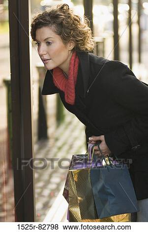 Young woman holding shopping bags and looking in the window of a shop View Large Photo Image Stock Photo - Young woman holding shopping bags and looking in the window of a shop. Fotosearch