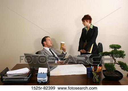 Businessman sitting in an office with his secretary standing beside him View Large Photo Image Stock Photo - Businessman sitting in an office with his secretary standing beside him. Fotosearch