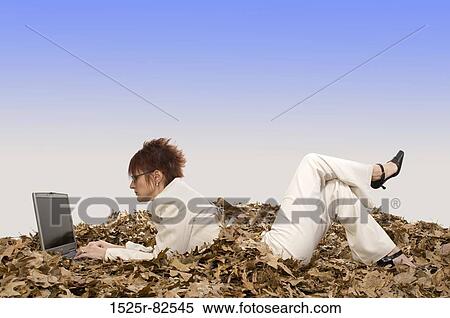 Businesswoman lying on dry leaves and working on a laptop View Large Photo Image Stock Photography - Businesswoman lying on dry leaves and working on a laptop. Fotosearch
