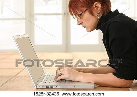 Stock Photograph - Businesswoman lying on the floor and working on a laptop. Fotosearch
