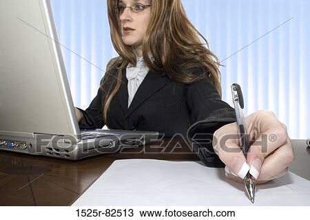 Businesswoman working on a laptop and writing on a sheet of paper View Large Photo Image Stock Image - Businesswoman working on a laptop and writing on a sheet of paper. Fotosearch