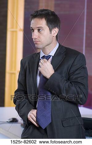 Businessman adjusting his tie in an office View Large Photo Image Stock Image - Businessman adjusting his tie in an office. Fotosearch