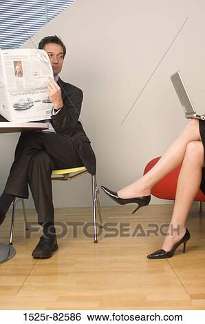Businessman holding a newspaper and looking at the legs of a businesswoman working on a laptop View Large Photo Image Stock Photograph - Businessman holding a newspaper and looking at the legs of a businesswoman working on a laptop. Fotosearch