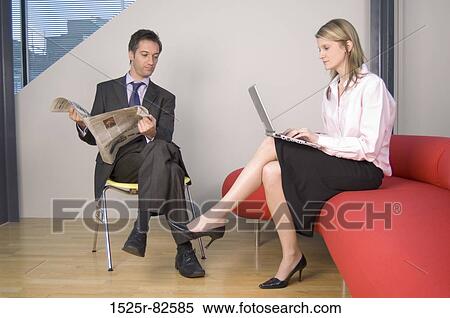 Businessman holding a newspaper and looking at the legs of a businesswoman working on a laptop View Large Photo Image Stock Photography - Businessman holding a newspaper and looking at the legs of a businesswoman working on a laptop. Fotosearch