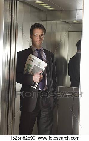 Businessman holding a newspaper in an elevator View Large Photo Image Stock Image - Businessman holding a newspaper in an elevator. Fotosearch