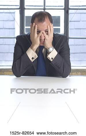 Businessman sitting at a table in an office View Large Photo Image Picture - Businessman sitting at a table in an office. Fotosearch