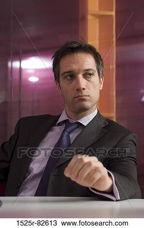 Businessman sitting at a table in an office View Large Photo Image Stock Image - Businessman sitting at a table in an office. Fotosearch