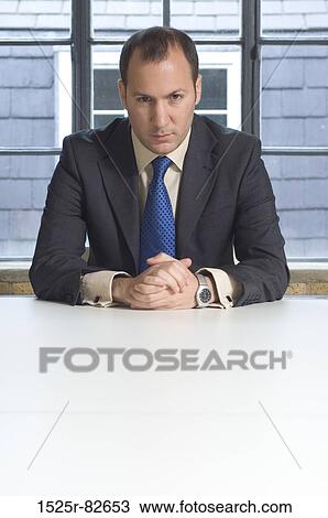 Businessman sitting at a table in an office View Large Photo Image Stock Image - Businessman sitting at a table in an office. Fotosearch