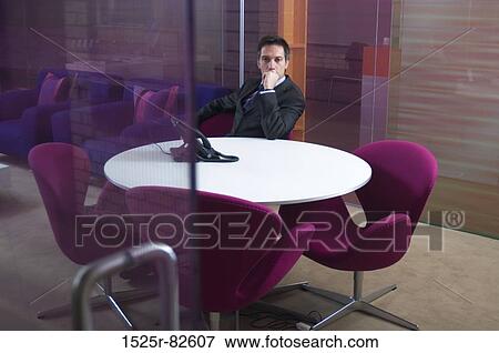 Businessman sitting at a table in an office View Large Photo Image Stock Photo - Businessman sitting at a table in an office. Fotosearch