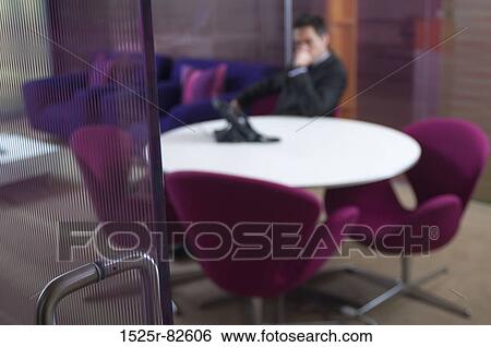 Businessman sitting at a table in an office View Large Photo Image Stock Photograph - Businessman sitting at a table in an office. Fotosearch