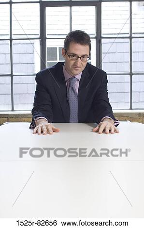 Businessman sitting at a table in an office View Large Photo Image Stock Photograph - Businessman sitting at a table in an office. Fotosearch