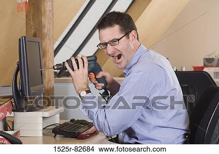Businessman sitting in front of a computer and holding a drill View Large Photo Image Picture - Businessman sitting in front of a computer and holding a drill. Fotosearch