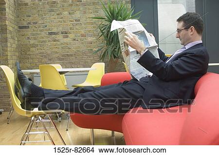 Businessman sitting on a couch and reading a newspaper View Large Photo Image Picture - Businessman sitting on a couch and reading a newspaper. Fotosearch