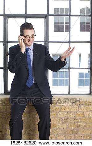 Businessman sitting on a window sill and talking on a mobile phone View Large Photo Image Stock Image - Businessman sitting on a window sill and talking on a mobile phone. Fotosearch
