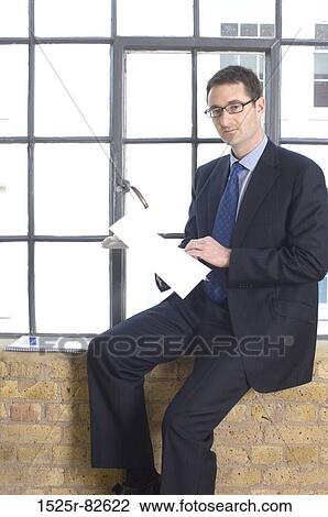Businessman sitting on a window sill and holding a document View Large Photo Image Stock Image - Businessman sitting on a window sill and holding a document. Fotosearch