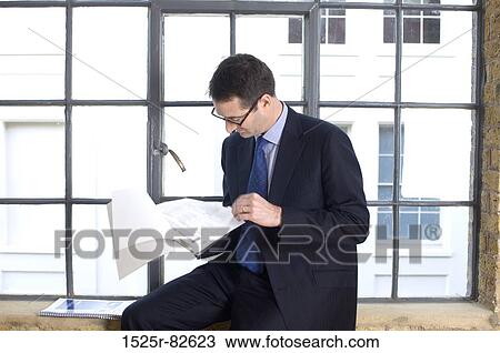 Businessman sitting on a window sill and reading documents View Large Photo Image Stock Image - Businessman sitting on a window sill and reading documents. Fotosearch