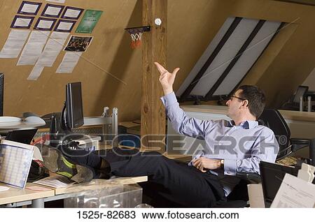 Businessman sitting on an office chair and throwing a crumpled paper ball in mini basketball hoop View Large Photo Image Stock Image - Businessman sitting on an office chair and throwing a crumpled paper ball in mini basketball hoop. Fotosearch
