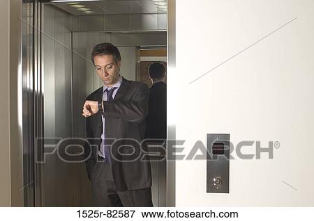 Businessman standing in an elevator and looking at his wristwatch View Large Photo Image Stock Photo - Businessman standing in an elevator and looking at his wristwatch. Fotosearch