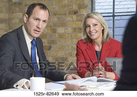 Businessman with a businesswoman sitting at a table in a meeting View Large Photo Image Stock Photo - Businessman with a businesswoman sitting at a table in a meeting. Fotosearch