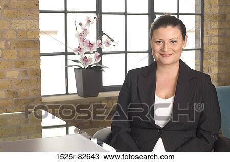 Businesswoman sitting at a table and smiling View Large Photo Image Stock Image - Businesswoman sitting at a table and smiling. Fotosearch