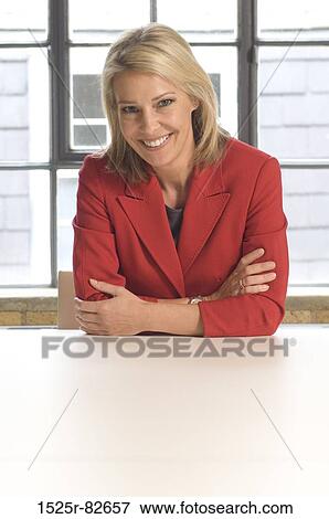 Businesswoman sitting at a table and smiling in an office View Large Photo Image Stock Photo - Businesswoman sitting at a table and smiling in an office. Fotosearch