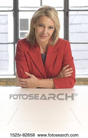 Businesswoman sitting at a table and smiling in an office View Large Photo Image Stock Photo - Businesswoman sitting at a table and smiling in an office. Fotosearch