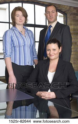 Businesswoman sitting at a table with two business executives standing behind her View Large Photo Image Picture - Businesswoman sitting at a table with two business executives standing behind her. Fotosearch