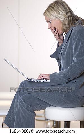 Businesswoman sitting on a stool and working on a laptop View Large Photo Image Stock Photo - Businesswoman sitting on a stool and working on a laptop. Fotosearch