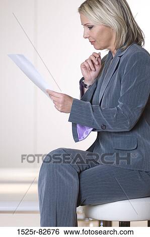 Stock Photograph - Businesswoman sitting on a stool reading documents. Fotosearch