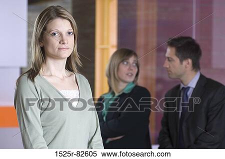Businesswoman standing in an office with two business executives in the background View Large Photo Image Stock Photography - Businesswoman standing in an office with two business executives in the background. Fotosearch