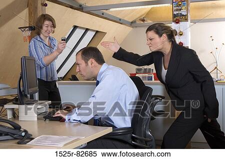 Stock Photography - Businesswoman taking a picture of her colleague making fun of a businessman behind his back. Fotosearch