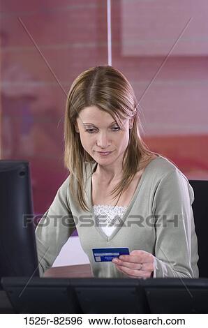 Stock Photograph - Mid adult woman sitting in front of a computer and holding a credit card. Fotosearch