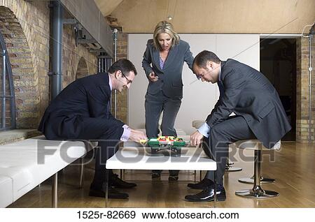 Two businessmen playing foosball with a businesswoman looking at them View Large Photo Image Stock Photo - Two businessmen playing foosball with a businesswoman looking at them. Fotosearch