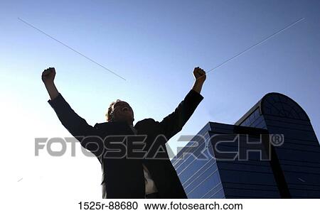 Business man holding up his arms in victory with a blue office building in the background View Large Photo Image Stock Image - Business man holding up his arms in victory with a blue office building in the background. Fotosearch